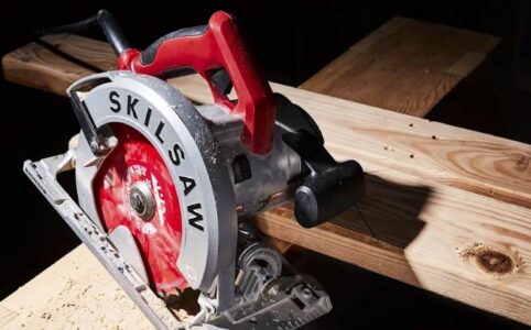 Close-up of a cordless circular saw mid-cut on plywood, showcasing blade depth adjustment.