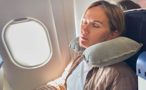 Woman sleeping peacefully on plane with twisted Dot&Dot travel pillow supporting her neck against window