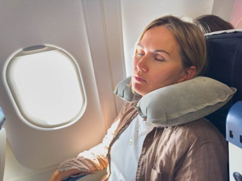 Woman sleeping peacefully on plane with twisted Dot&Dot travel pillow supporting her neck against window