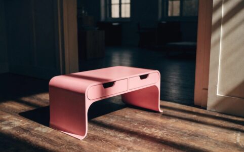 Small console table with drawers in pink styled in a modern entryway with mirror and decorative accents